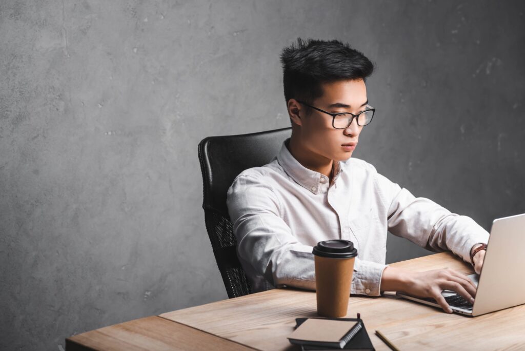 asian seo manager sitting at table and using laptop